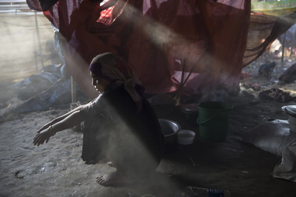 THAINKHALI, BANGLADESH - SEPTEMBER 25: Sajida Begum, 18, sits in her makeshift tent, washing rice for dinner as smoke catches the late afternoon light September 25, 2017 in Thainkhali camp, Cox's Bazar, Bangladesh. Over 429,000 Rohingya refugees have fled into Bangladesh since late August during the outbreak of violence in Rakhine state as Myanmar's de facto leader Aung San Suu Kyi downplayed the crisis during a speech in Myanmar this week faces and defended the security forces while criticism on her handling of the Rohingya crisis grows. Bangladesh's prime minister, Sheikh Hasina, spoke at the United Nations General Assembly last week, focusing on the humanitarian challenges of hosting the minority Muslim group who currently lack food, medical services, and toilets, while new satellite images from Myanmar's Rakhine state continue to show smoke rising from Rohingya villages. (Photo by Paula Bronstein/Getty Images)